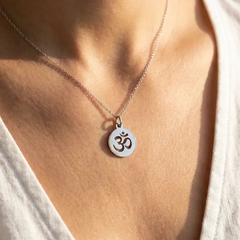 Silver necklace with a pendant featuring an Om symbol on a person's neck.