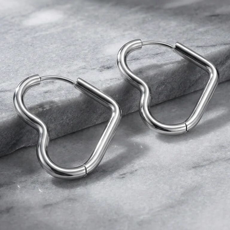 Pair of heart shaped silver hoop earrings on a gray stone surface