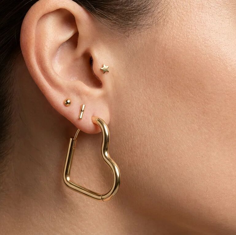Close-up of an ear with gold hoop earrings and small studs.