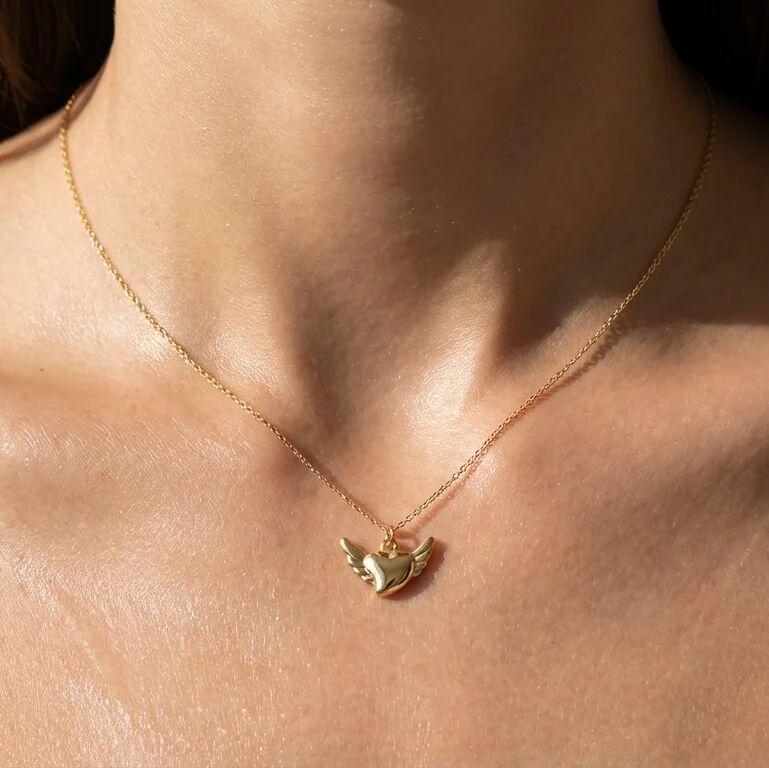 Gold necklace with a heart and wing pendant on a person's neck