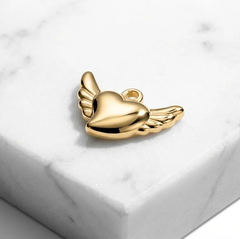 Gold heart-shaped pendant with wings on a white marble surface