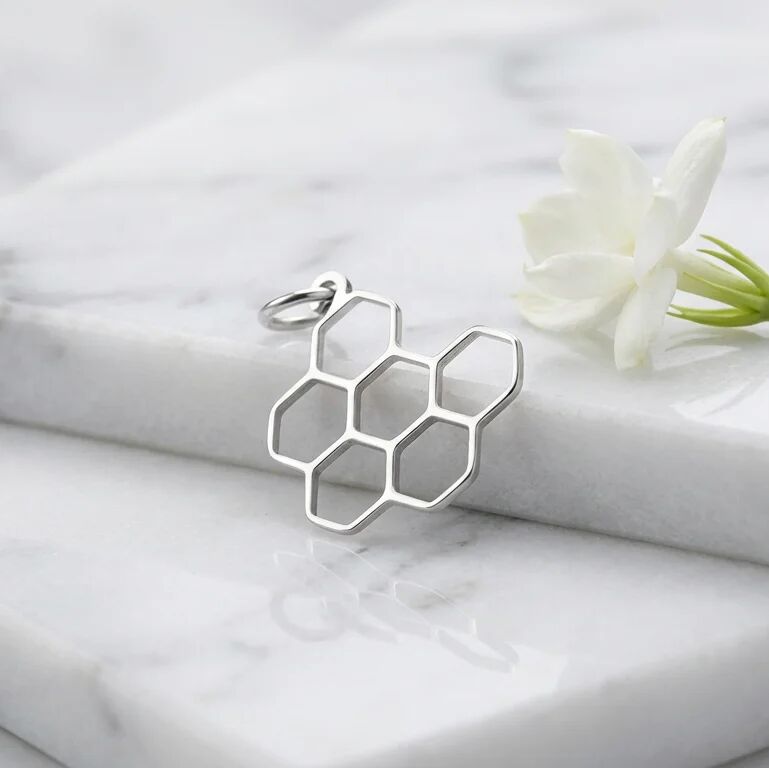 Silver honeycomb pendant on a marble surface with a white flower