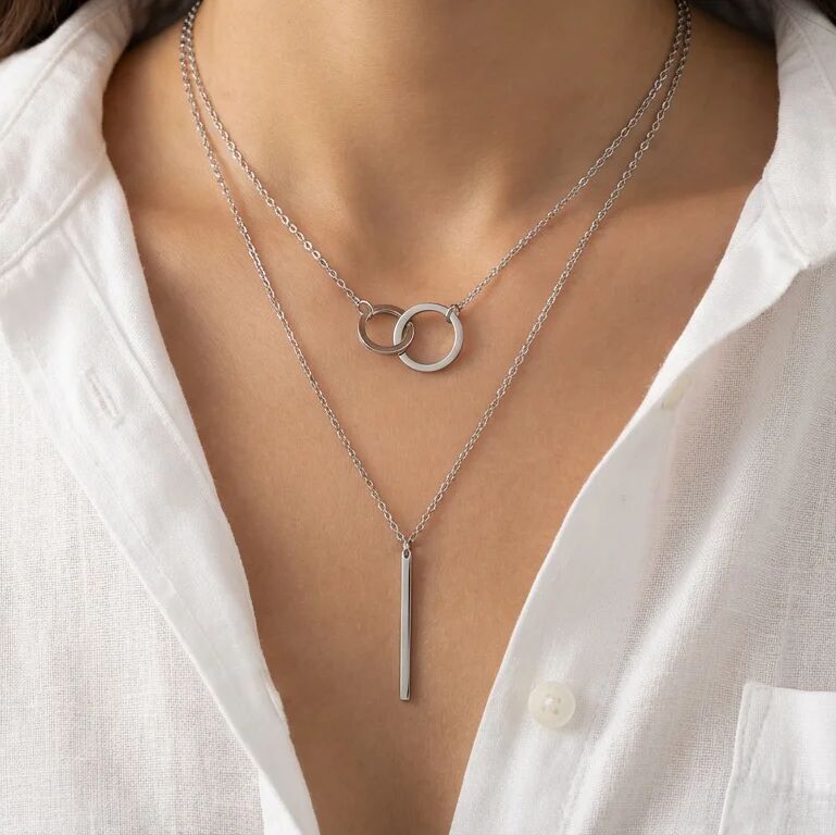 Silver necklace with interlocking rings and a vertical bar on a white shirt background