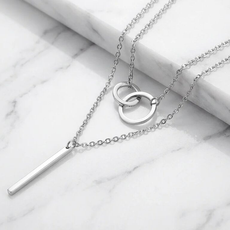 Silver necklace with interlocking rings and a bar pendant on a marble surface