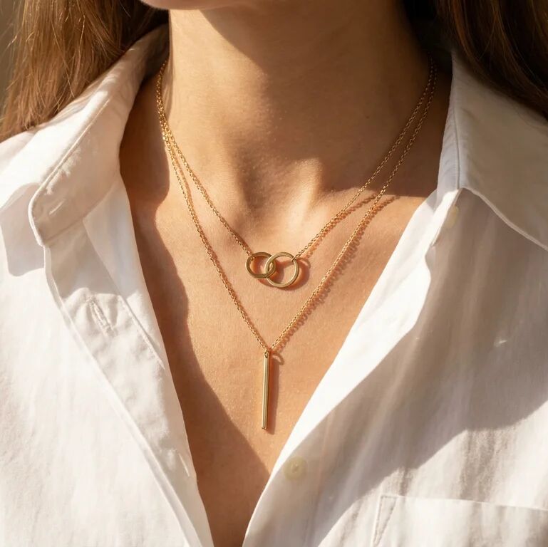 Close-up of a person wearing a gold necklace with interlocking rings on a white shirt.