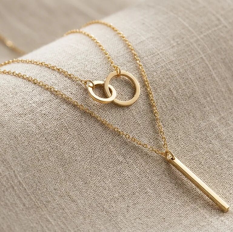 Gold necklace with interlocking rings and a bar pendant on a beige fabric background