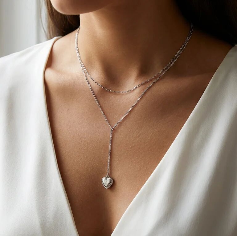 Silver necklace with a heart pendant worn by a person in a white top.