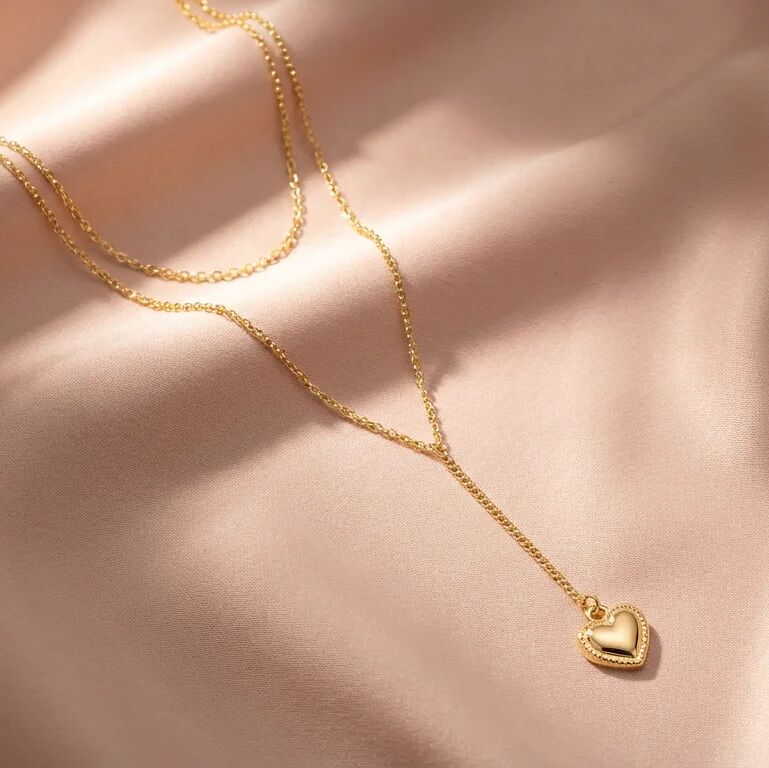 Gold heart-shaped pendant necklace on a soft pink background
