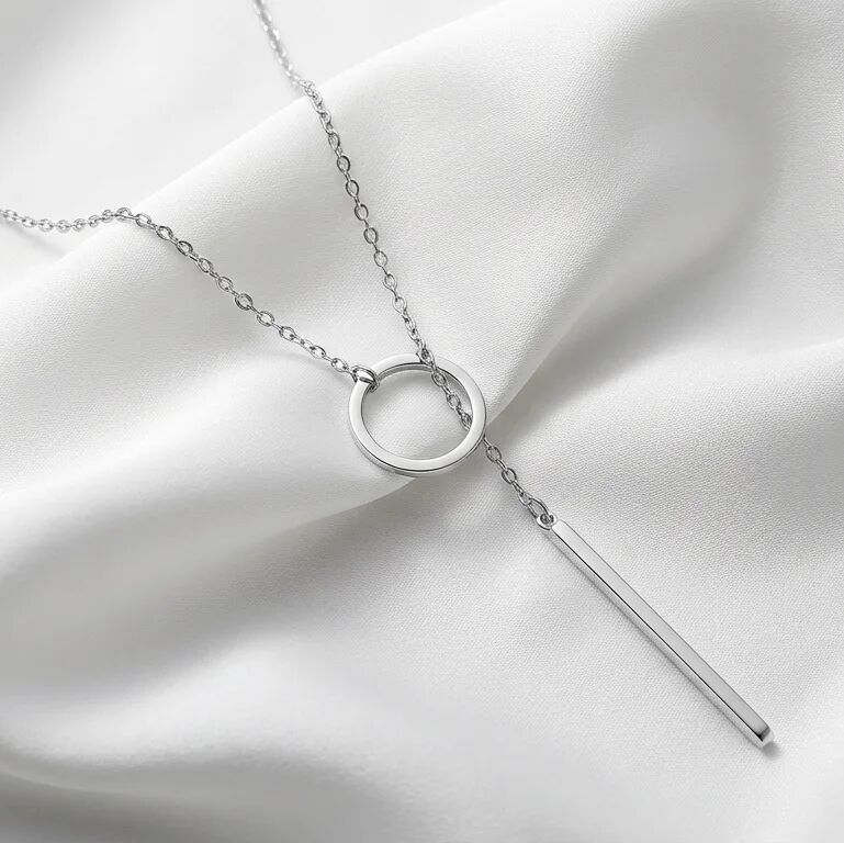 Silver necklace with a circular pendant and a bar on a white fabric background