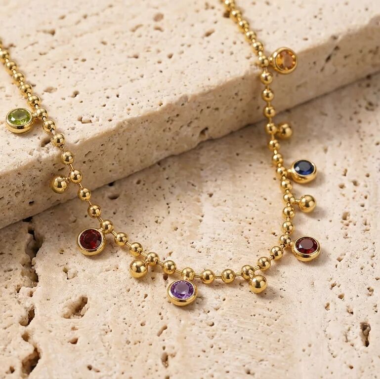 Gold necklace with colorful gemstones on a textured stone surface