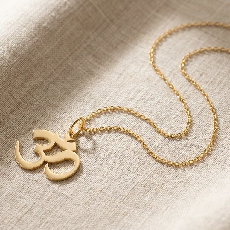 Gold Om symbol necklace on a textured beige fabric background