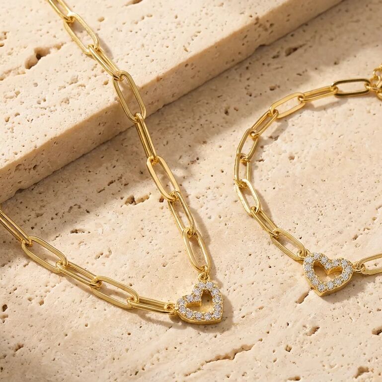 Gold chain necklace with heart-shaped pendants on a textured beige surface