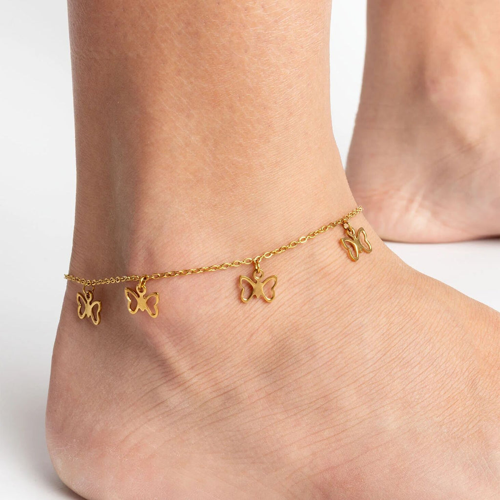Gold butterfly anklets on a person's ankles against a white background