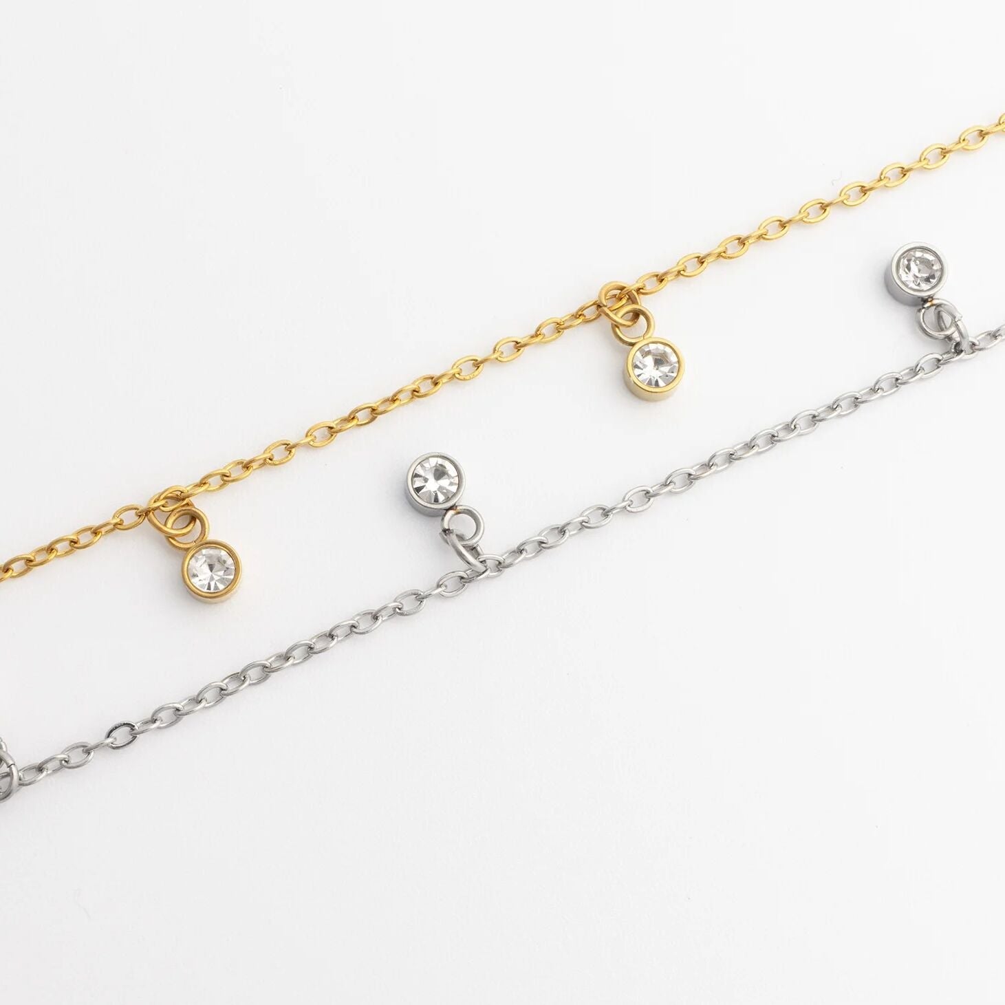 Two gold and silver anklets with small round stones on a white background