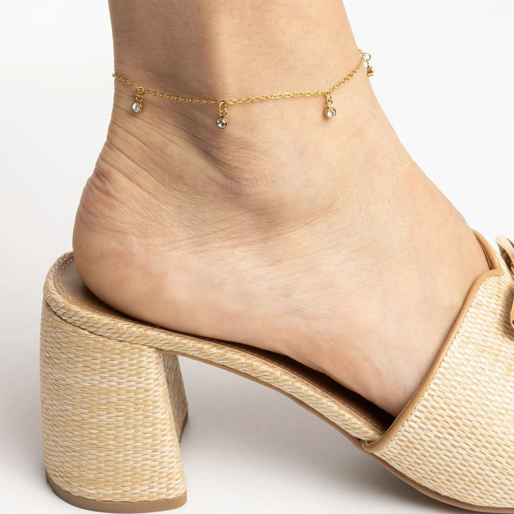 Beige sandal worn on a foot with a gold anklet against a light background
