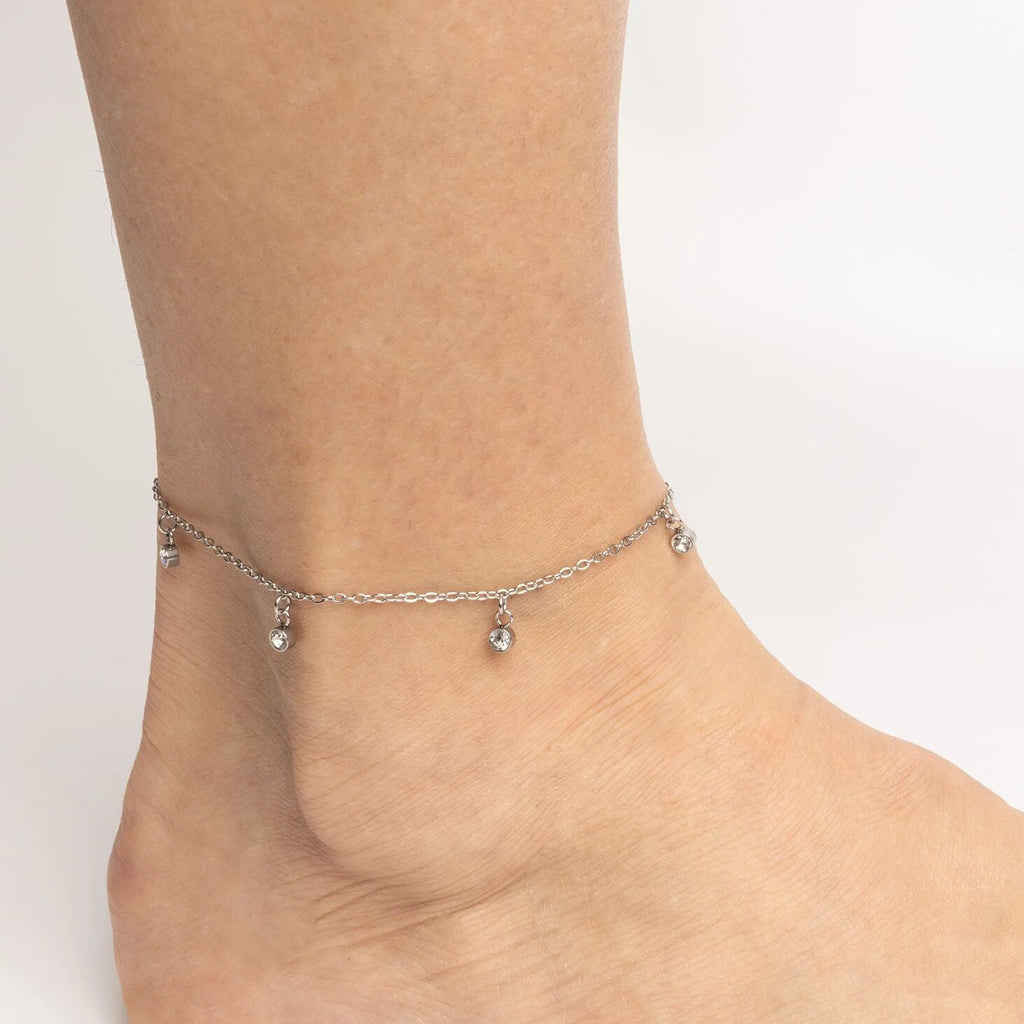 Silver anklet with small beads on a person's ankle against a light background