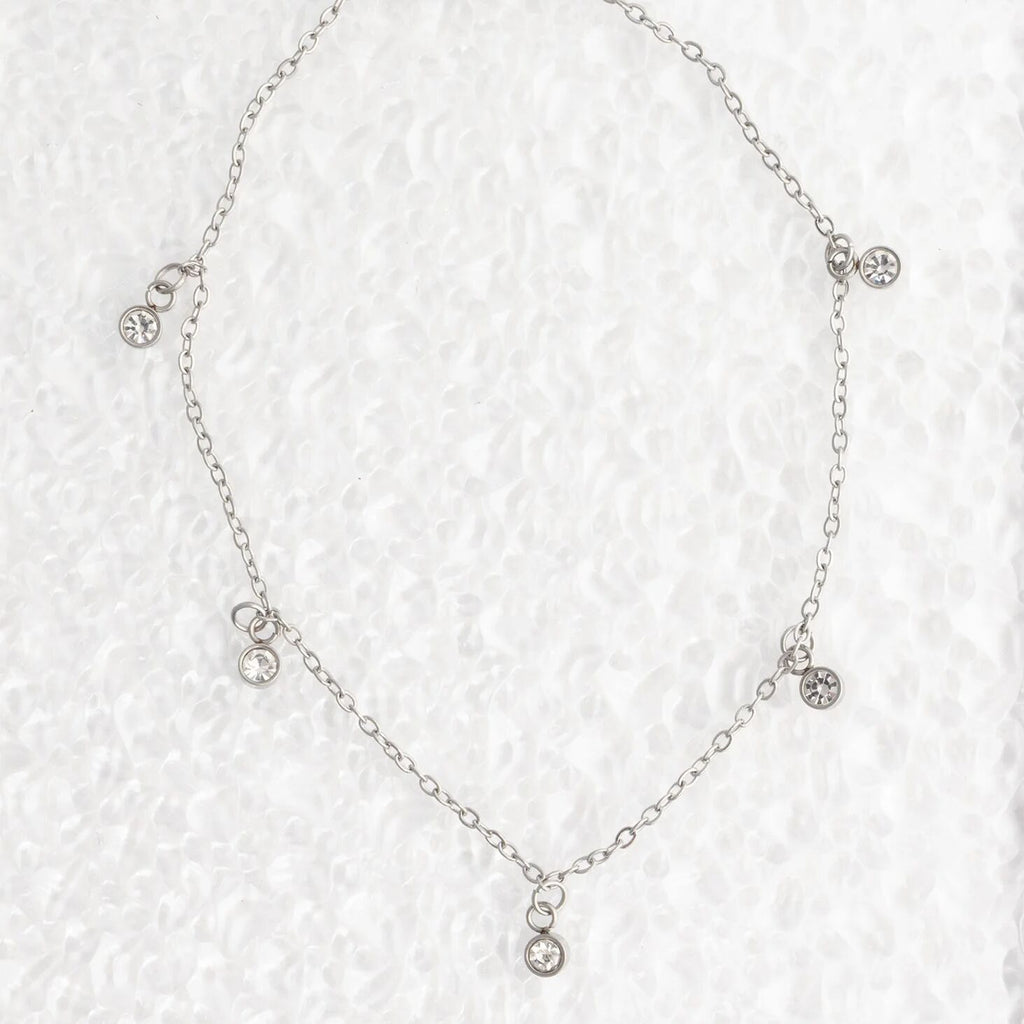 Silver necklace with small crystals on a textured white background