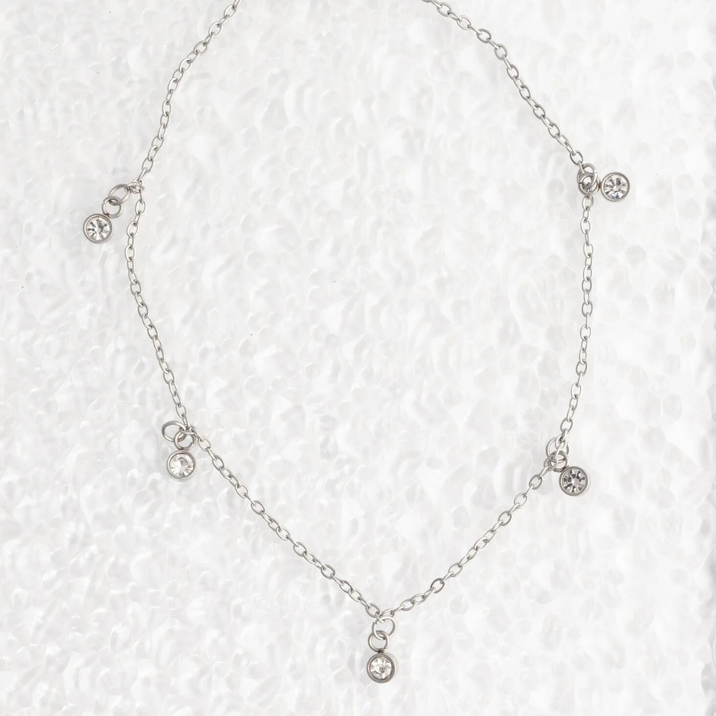 Silver necklace with small crystals on a textured white background