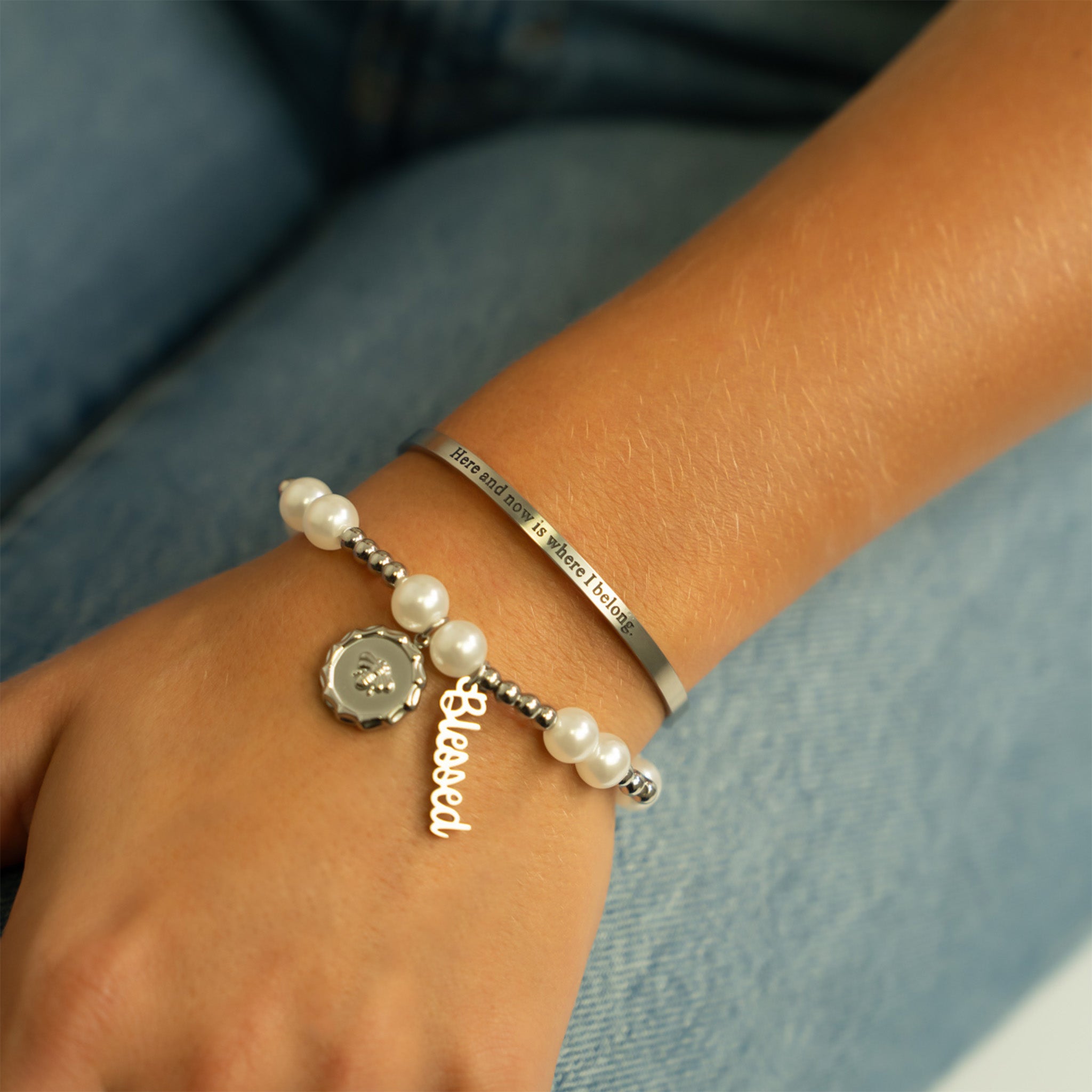 Bracelet with pearls and a charm on a wrist against a denim background