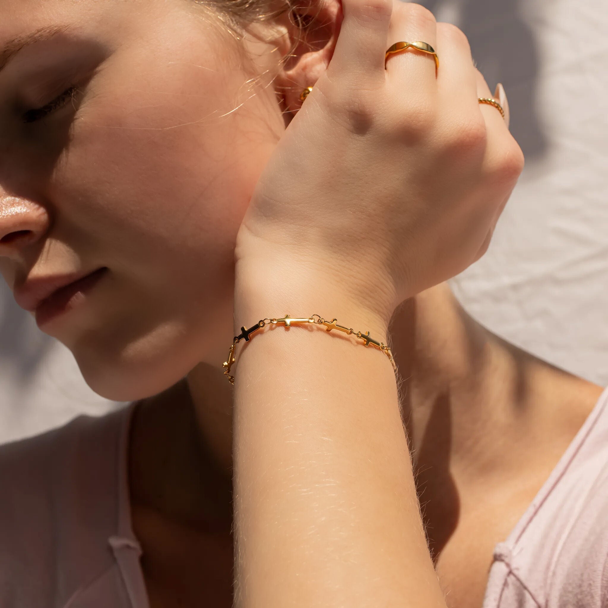 Close-up of a person wearing gold jewelry including an earring, cross bracelet, and ring.