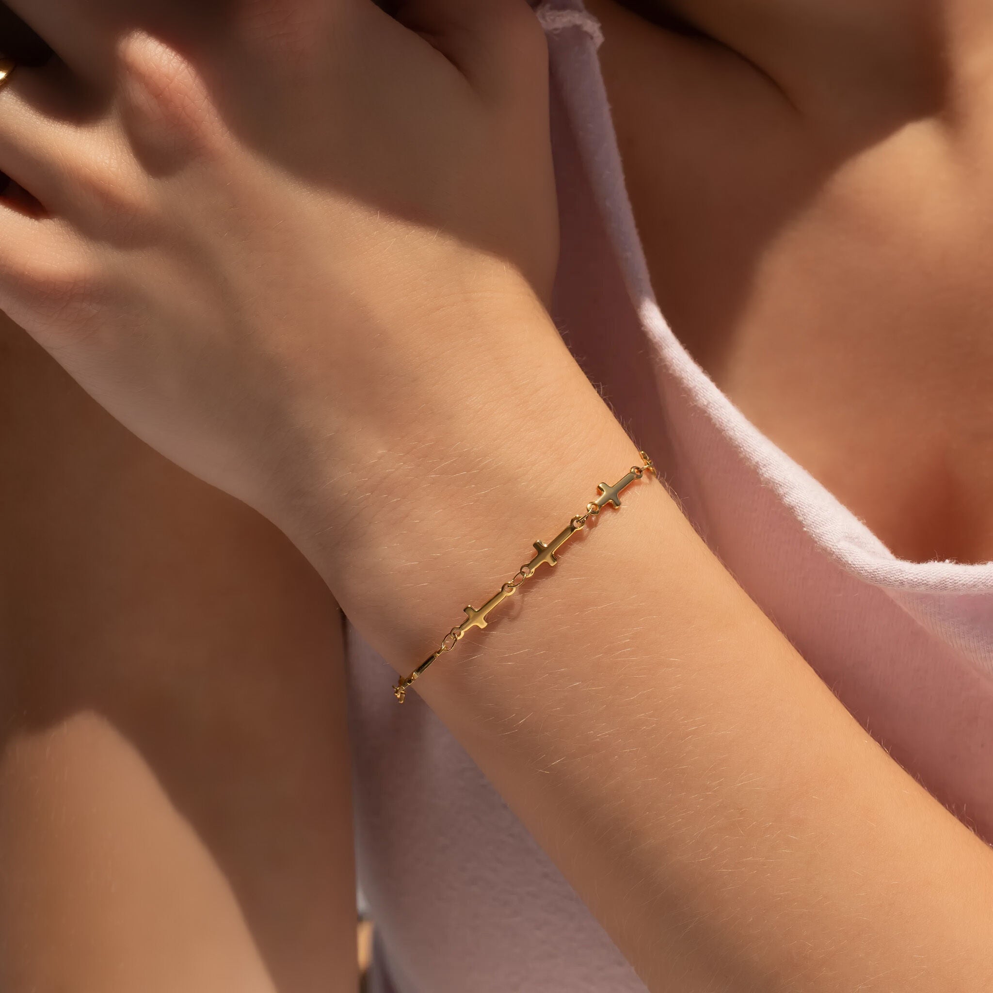 Gold cross bracelet on a wrist with a blurred background