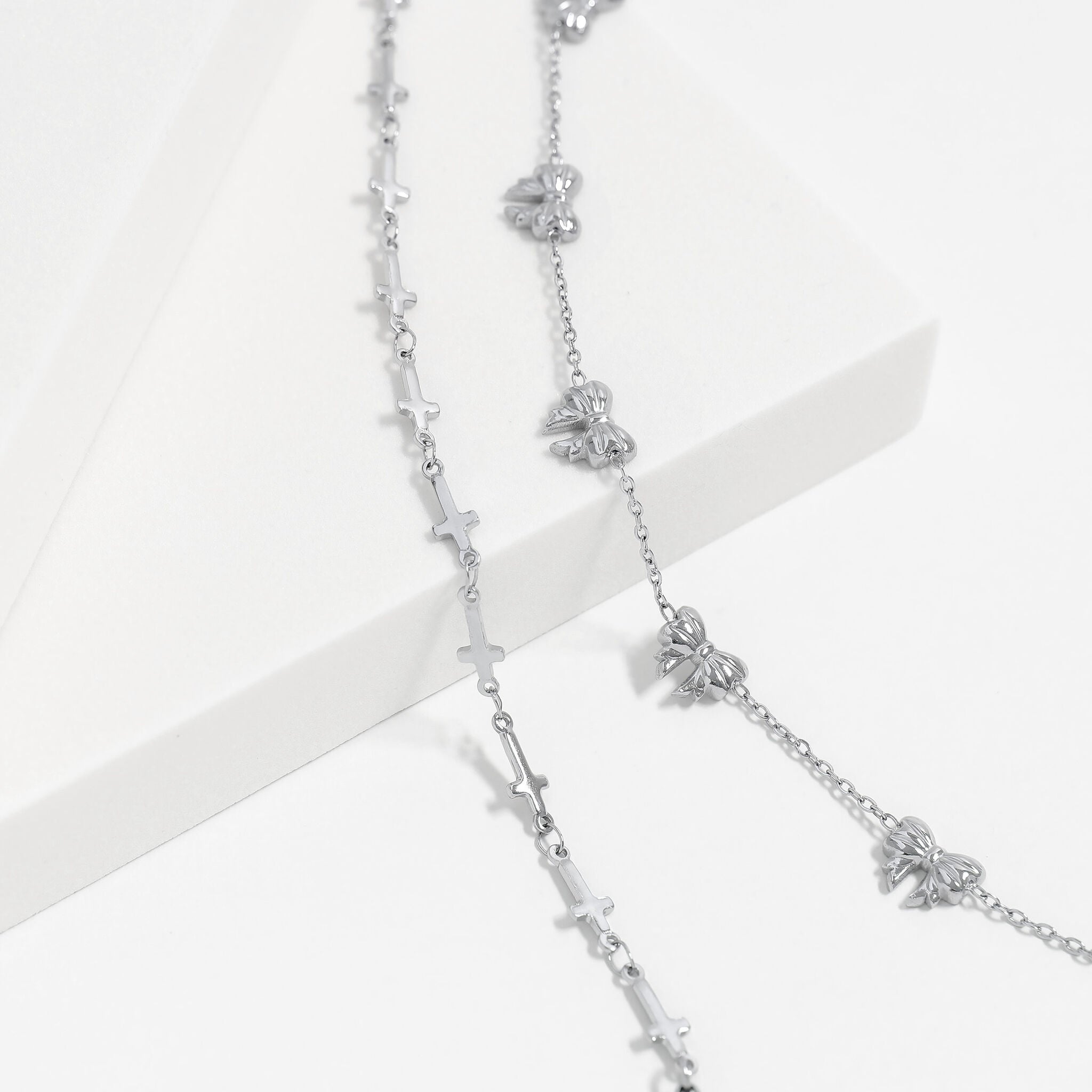 Silver necklace with bow and cross pendants on a white background
