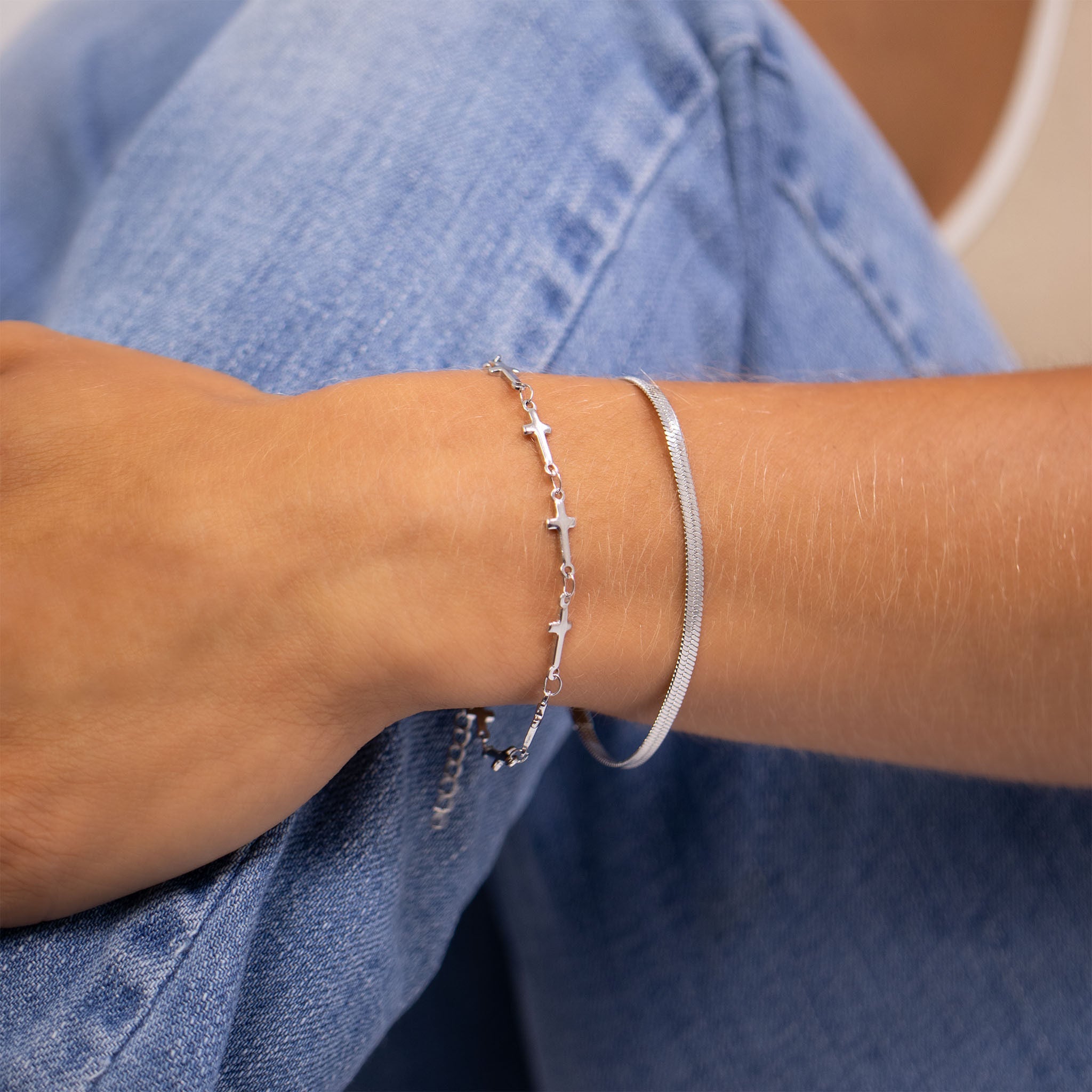 Silver cross bracelet on a wrist with a denim background