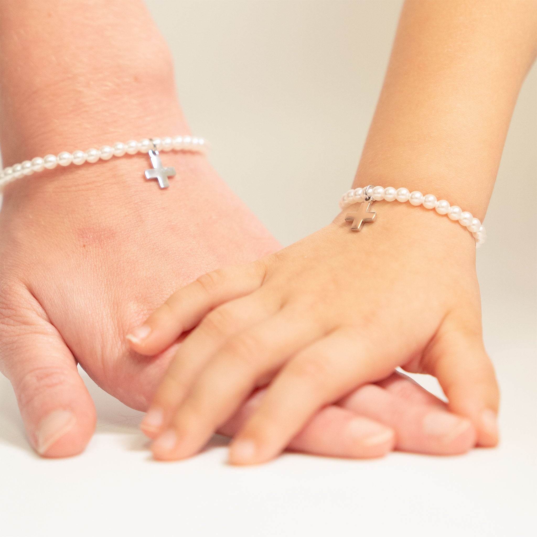 Two hands wearing pearl bracelets with small crosses on a light background