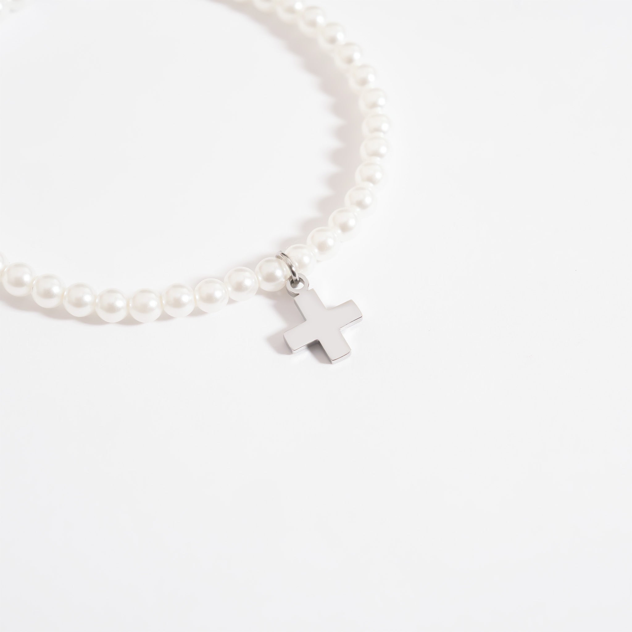 Pearl bracelet with a silver cross charm on a white background