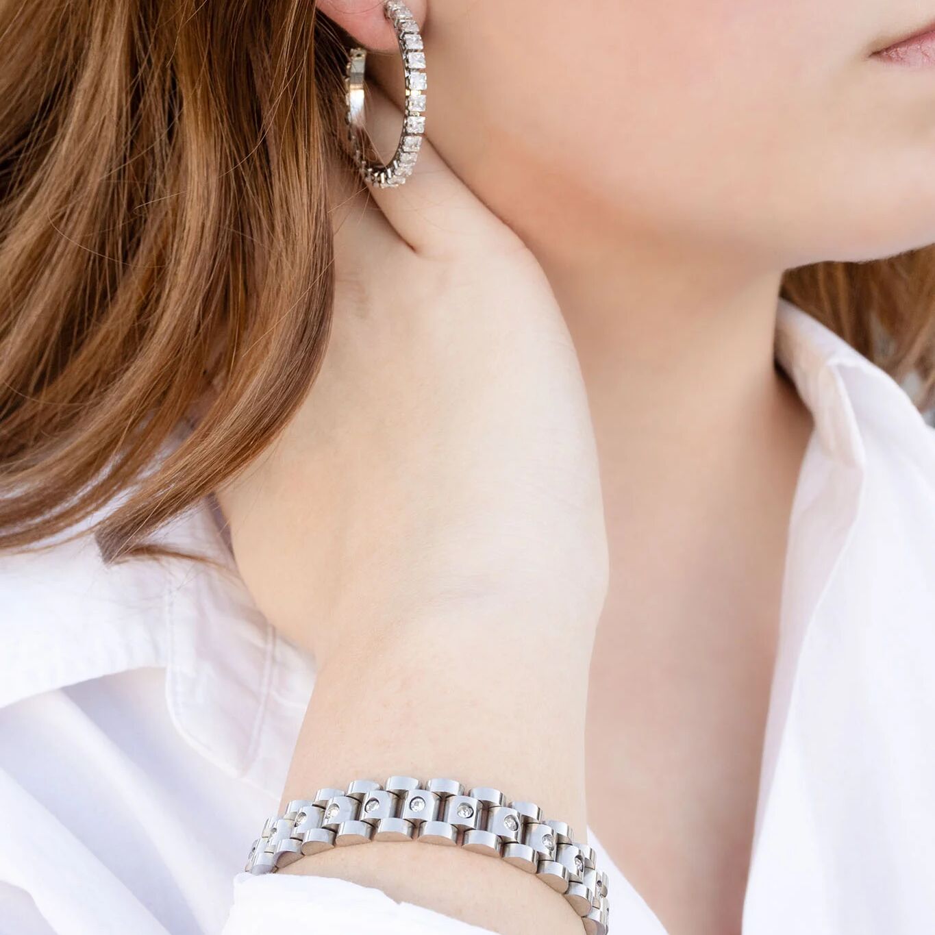 Close-up of a person wearing silver hoop earrings and bracelet.