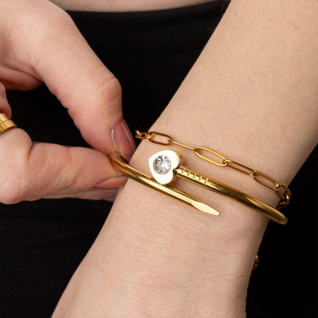 Gold bracelet with a heart-shaped charm being adjusted on a wrist against a black background