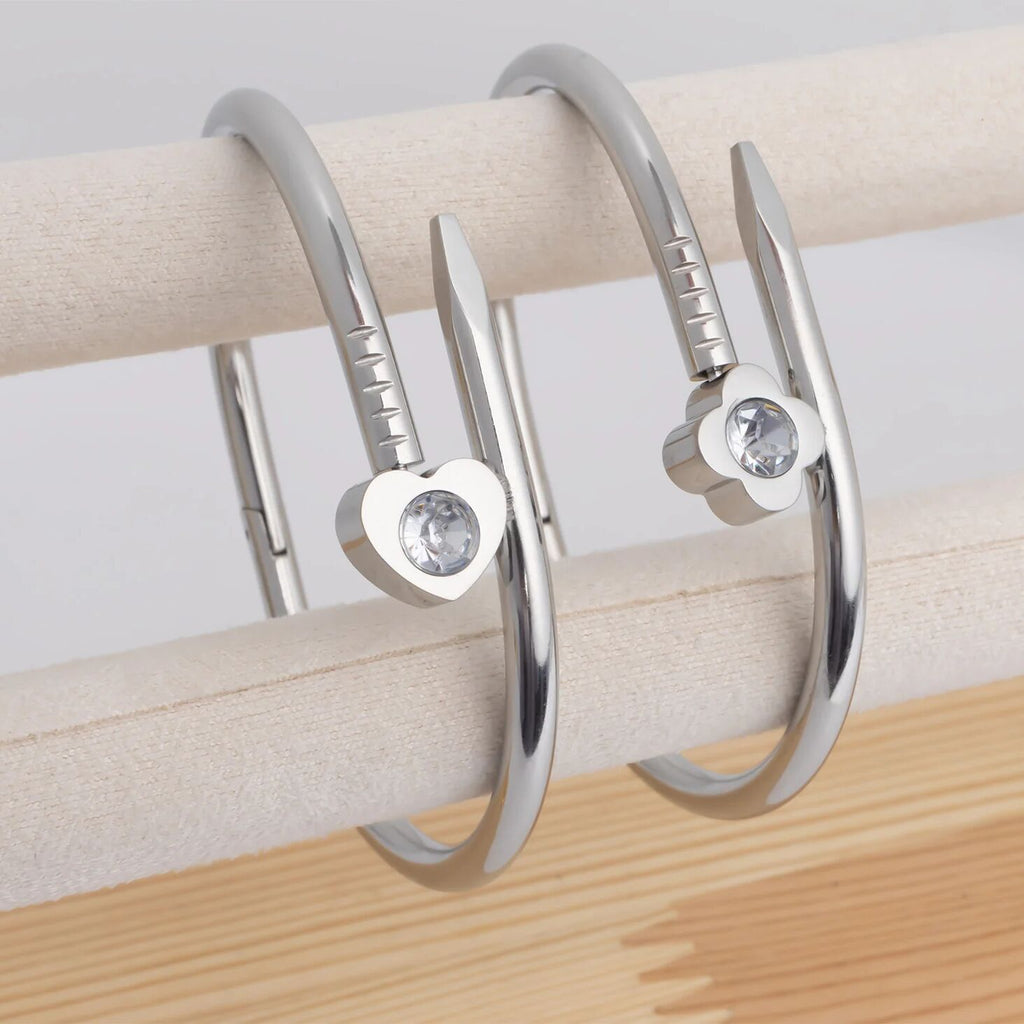 Three silver hoop earrings with heart-shaped gemstones on a wooden surface.