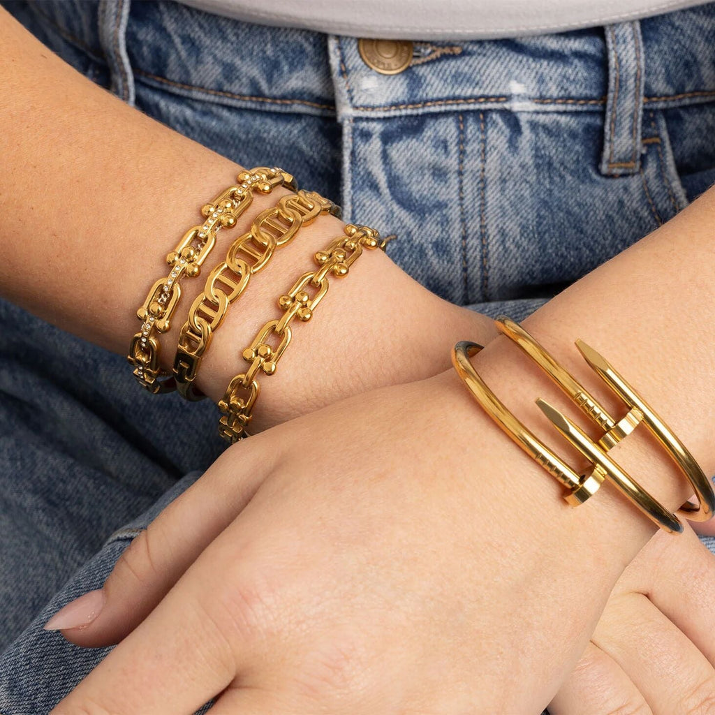 Gold chain bracelet and gold cuff on a wrist with denim background