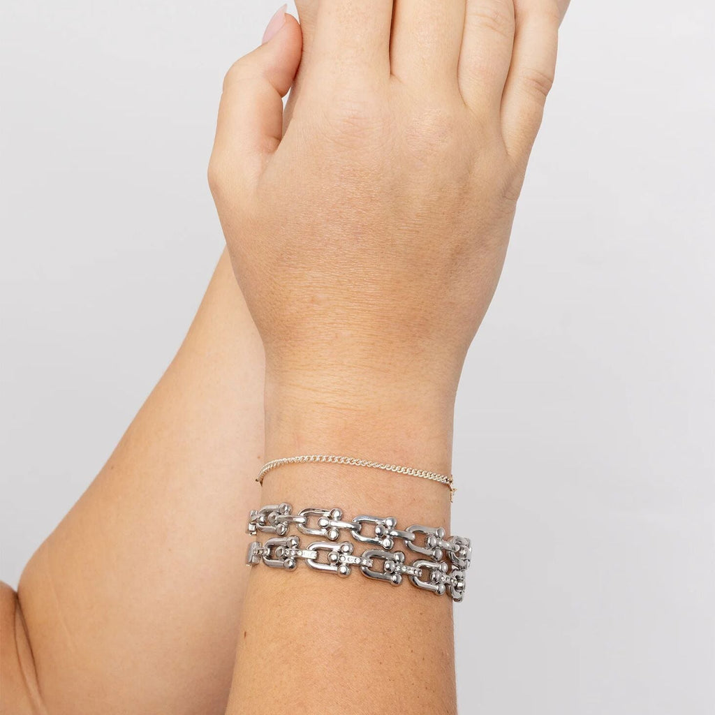 Silver chain bracelet on a wrist against a plain background