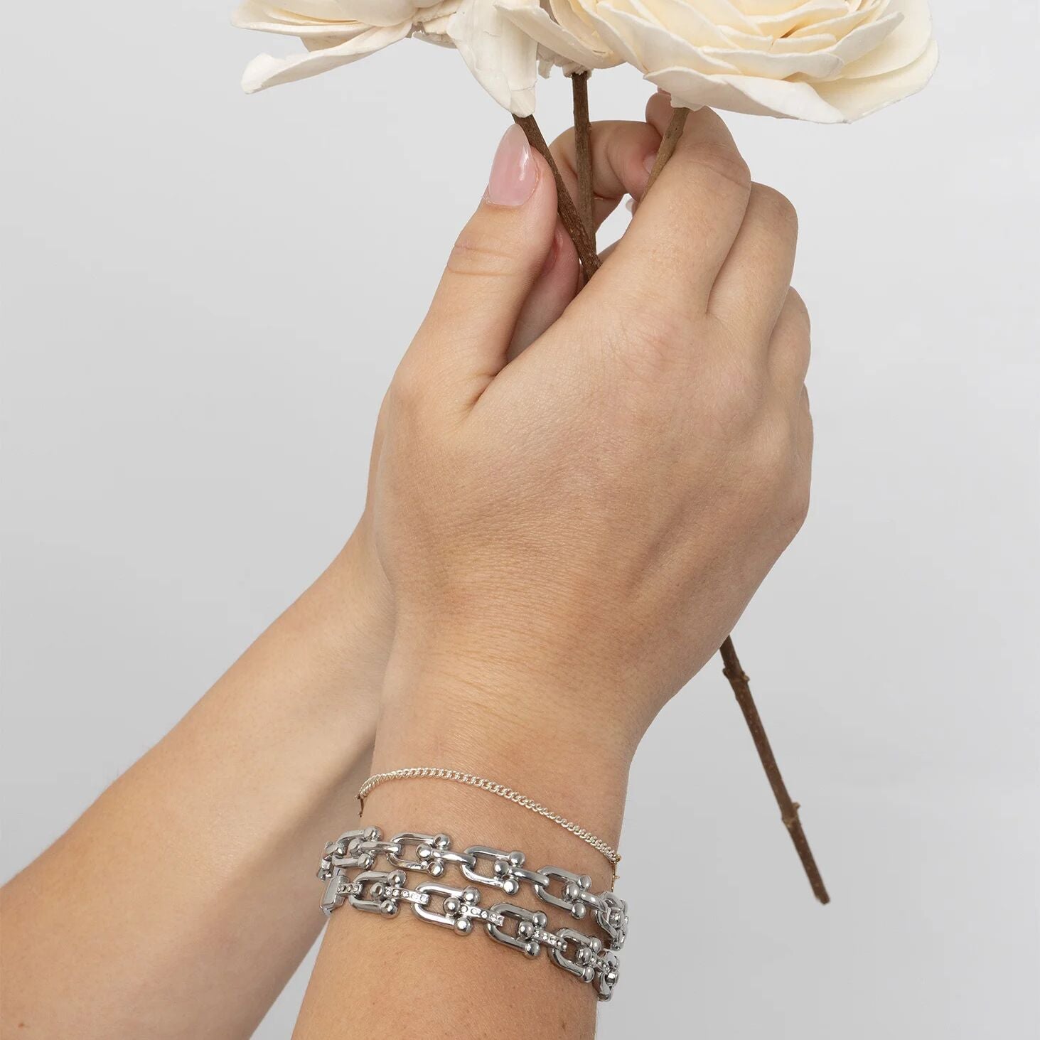 Hand holding flowers with silver chain bracelet on a light gray background