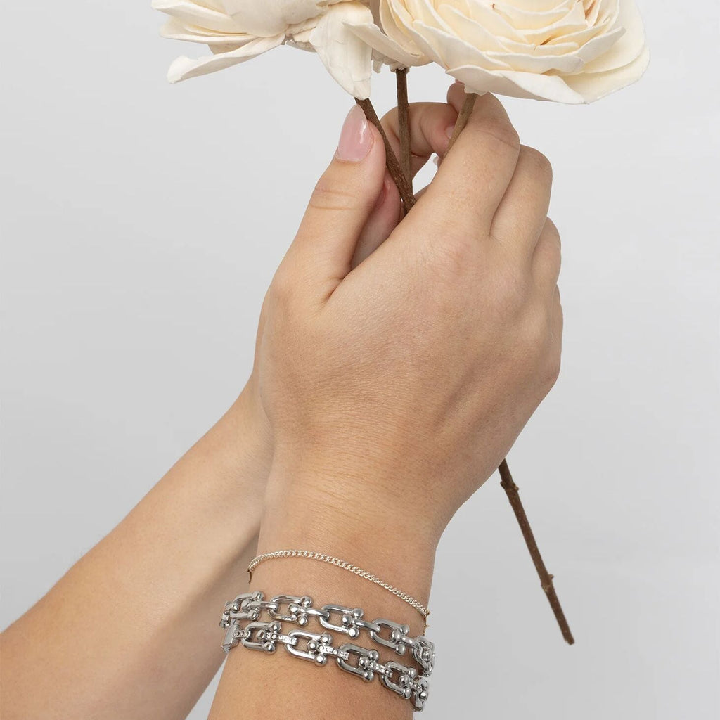 Hand holding a bouquet of white flowers with silver bracelets on a light gray background