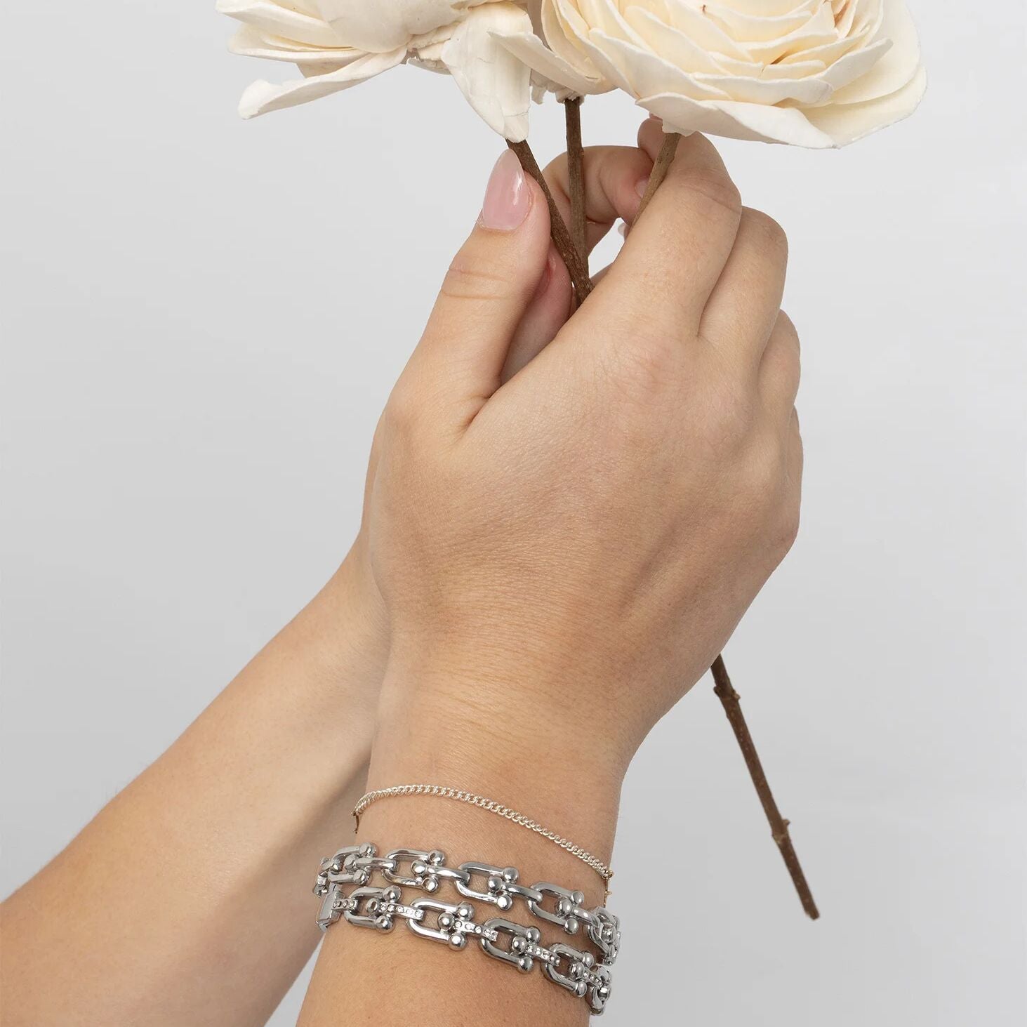 Hand holding a bouquet of white flowers with silver bracelets on a light gray background