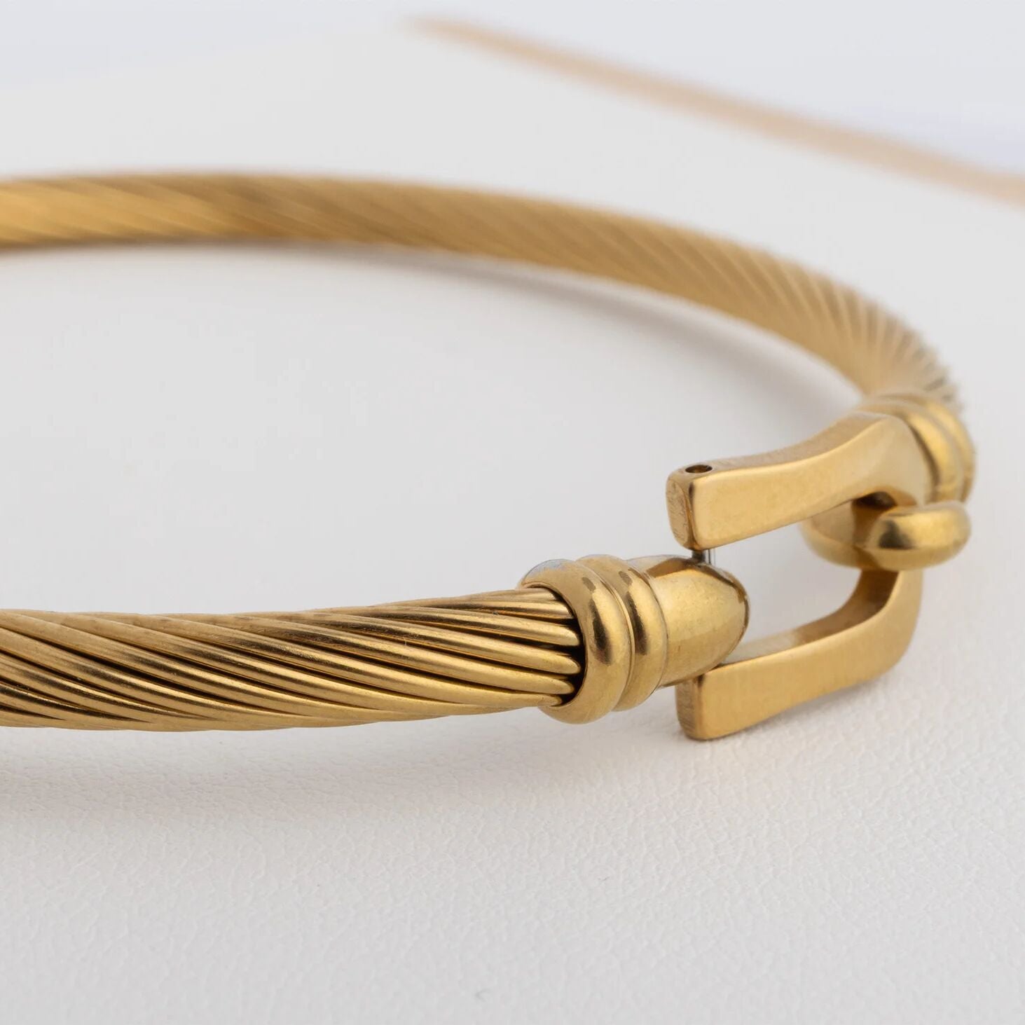 Gold bracelet with a clasp on a light gray background