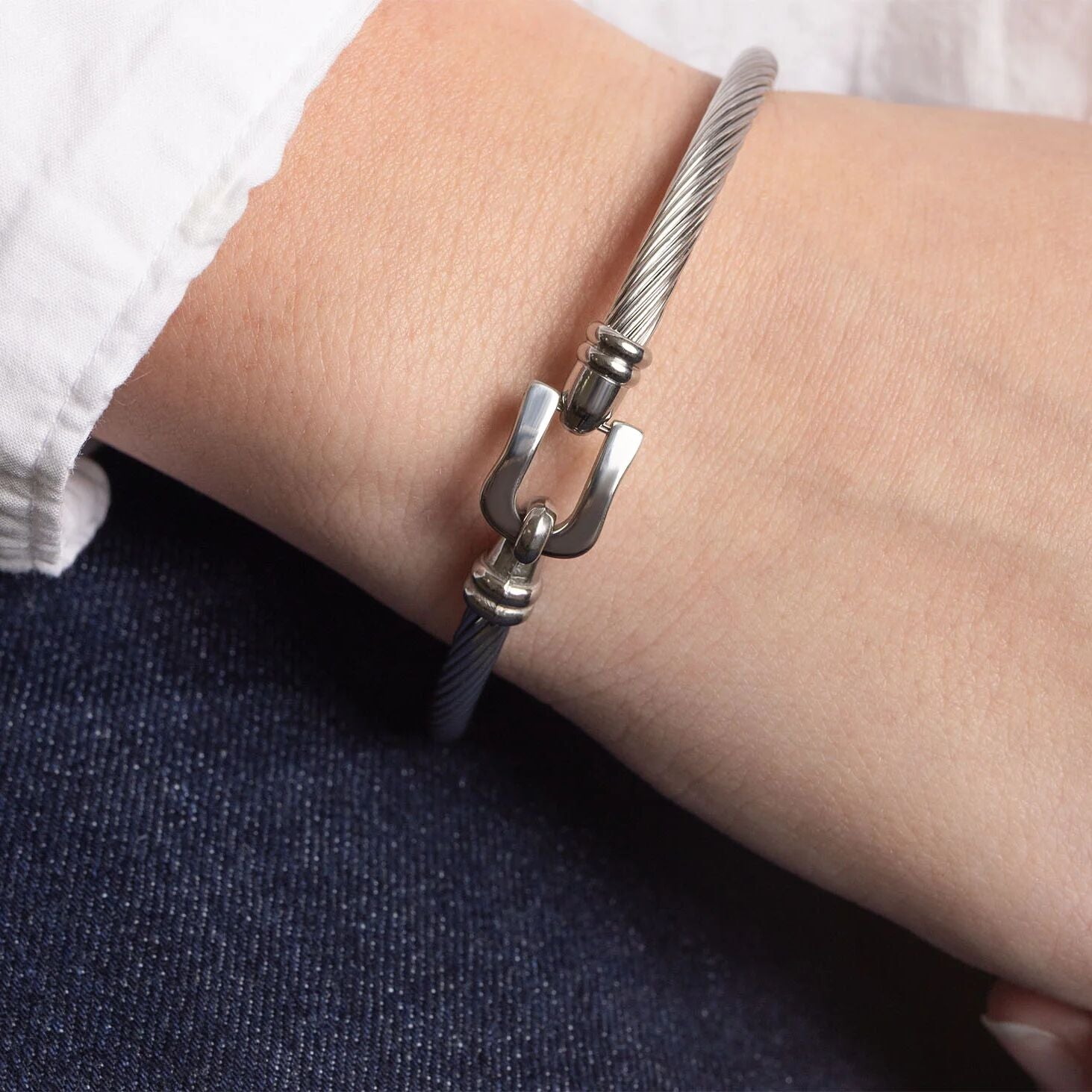Silver bracelet with a unique clasp on a wrist against a white shirt and dark jeans background