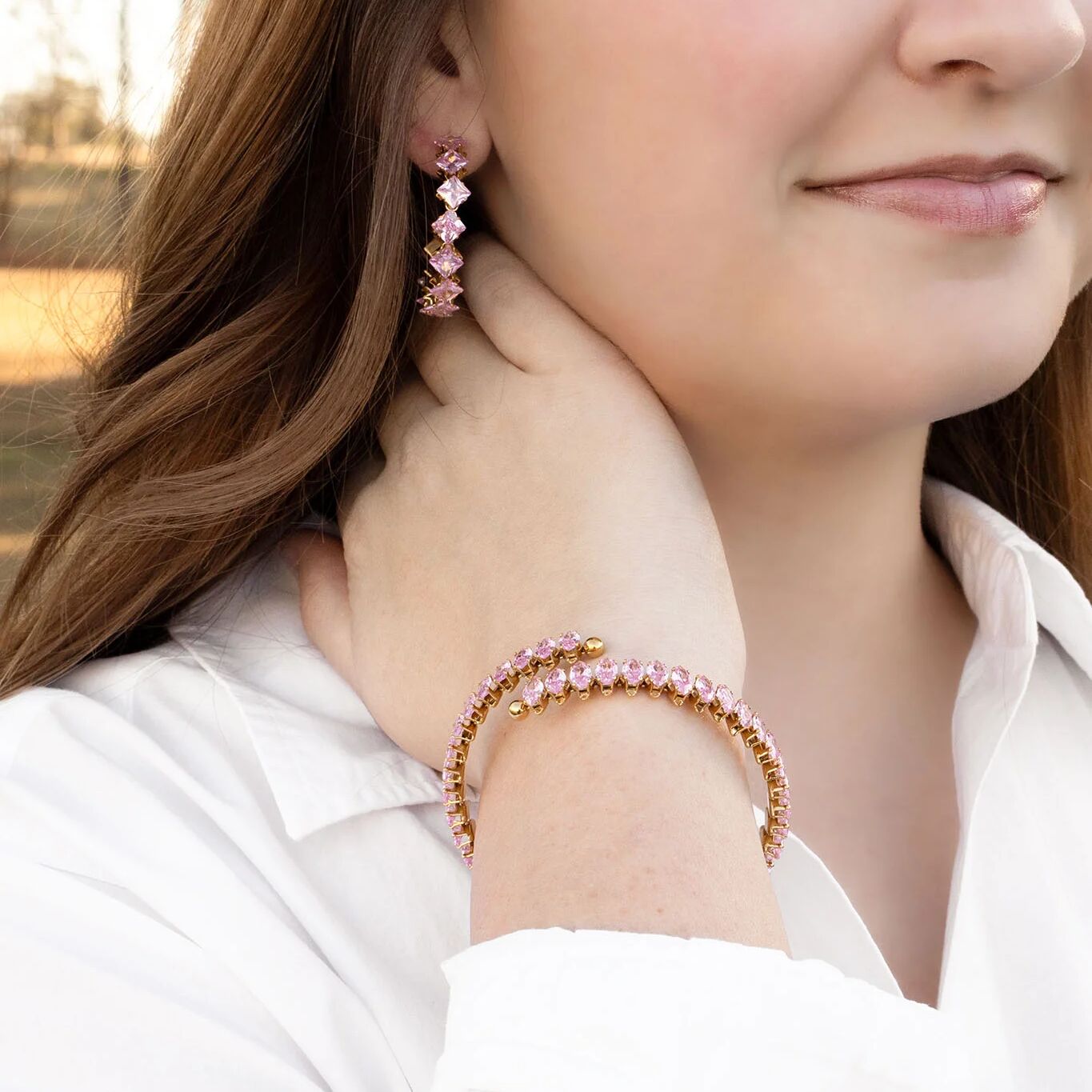 Close-up of a woman wearing pink beaded earrings and bracelet outdoors.