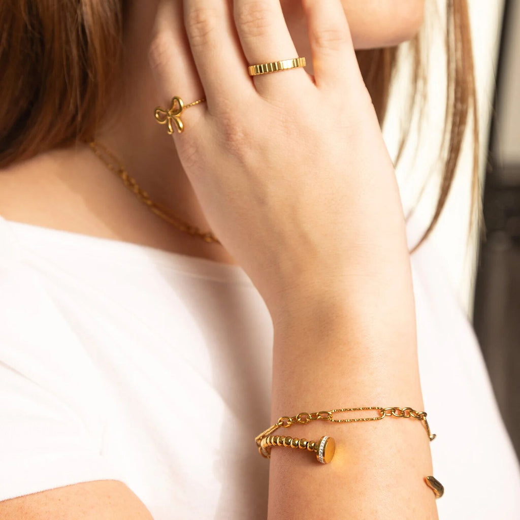 Close-up of a person wearing gold jewelry including an earring, ring, and bracelet.