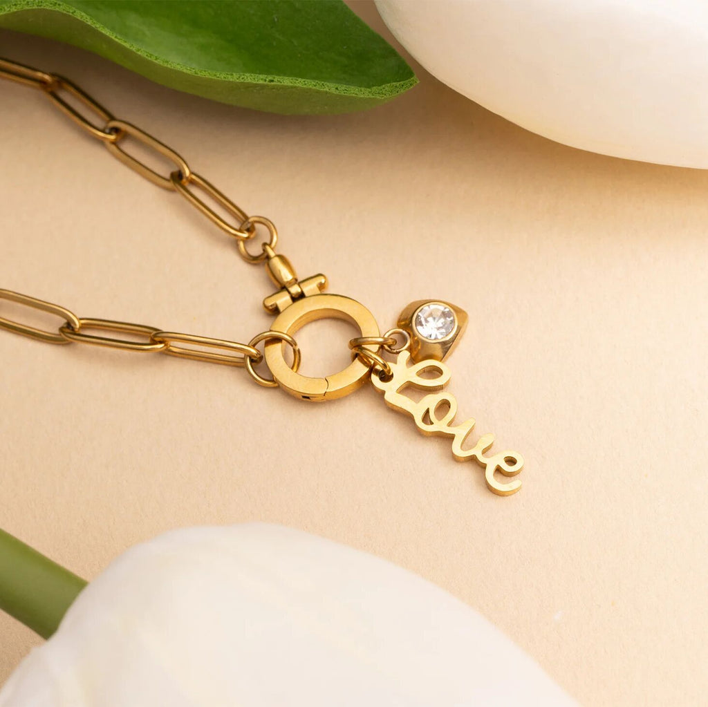 Gold necklace with 'love' charm on a beige background