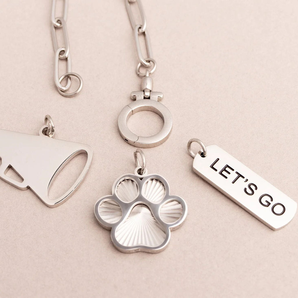 Silver dog tag with paw print design and 'LET'S GO' tag on a beige background