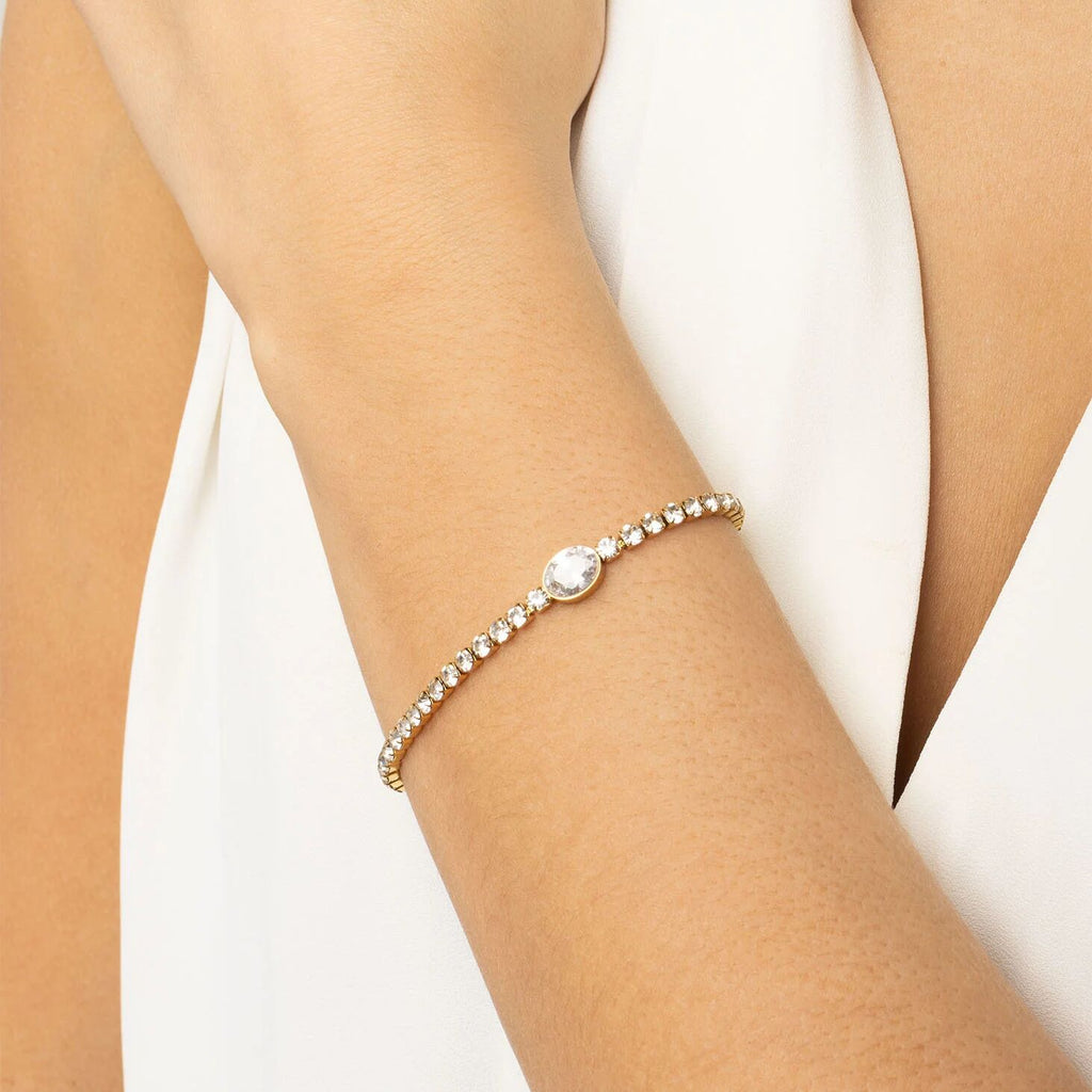 Gold bracelet with a central gemstone on a person's wrist against a white background