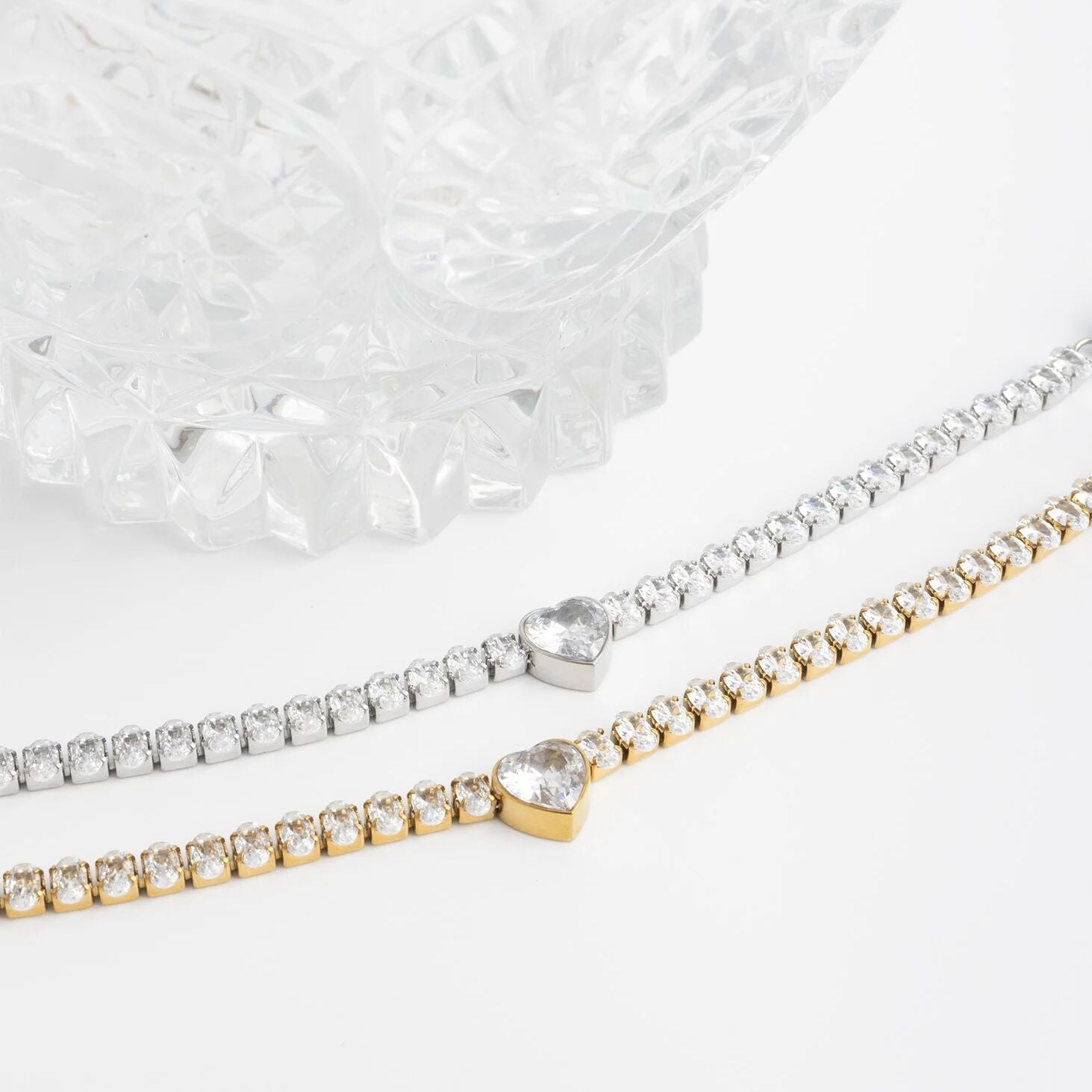 Two bracelets, one gold and one silver, with heart-shaped gemstones on a white background.