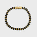 Black beaded bracelet with gold clasp on a light gray background