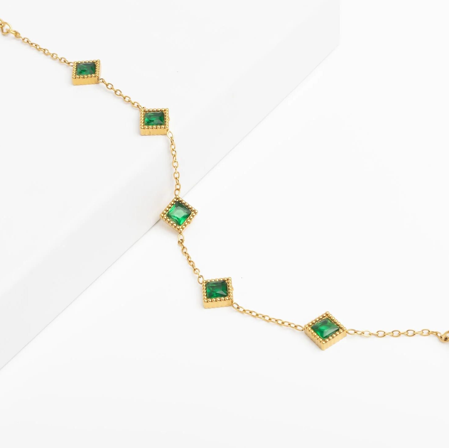 Gold necklace with green gemstones on a white background