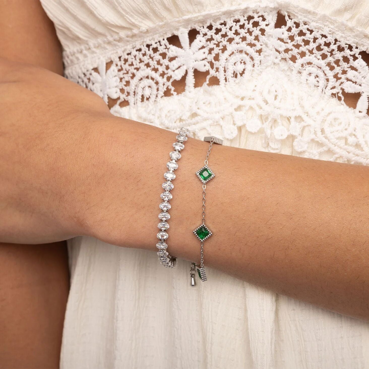 Two bracelets with green gemstones on a person's wrist against a white lace background