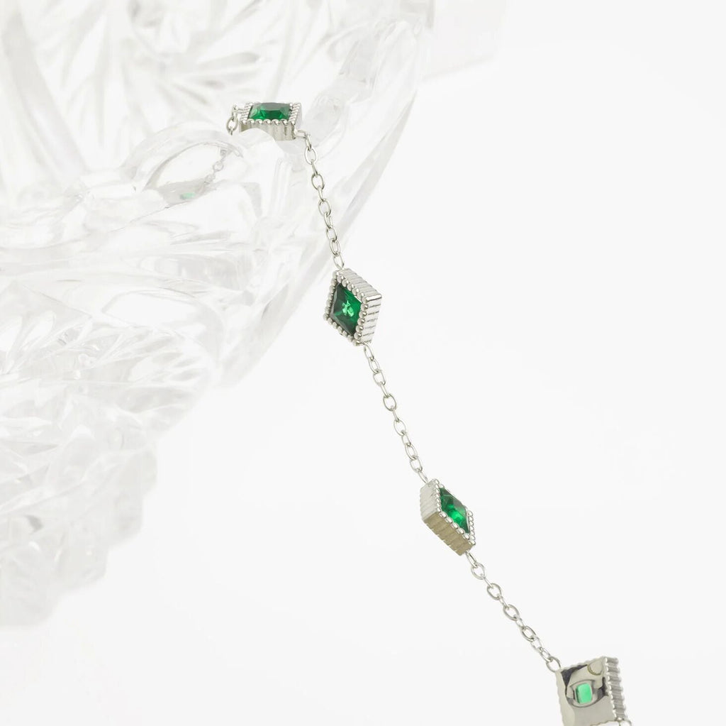 Silver bracelet with green gemstones on a textured white surface