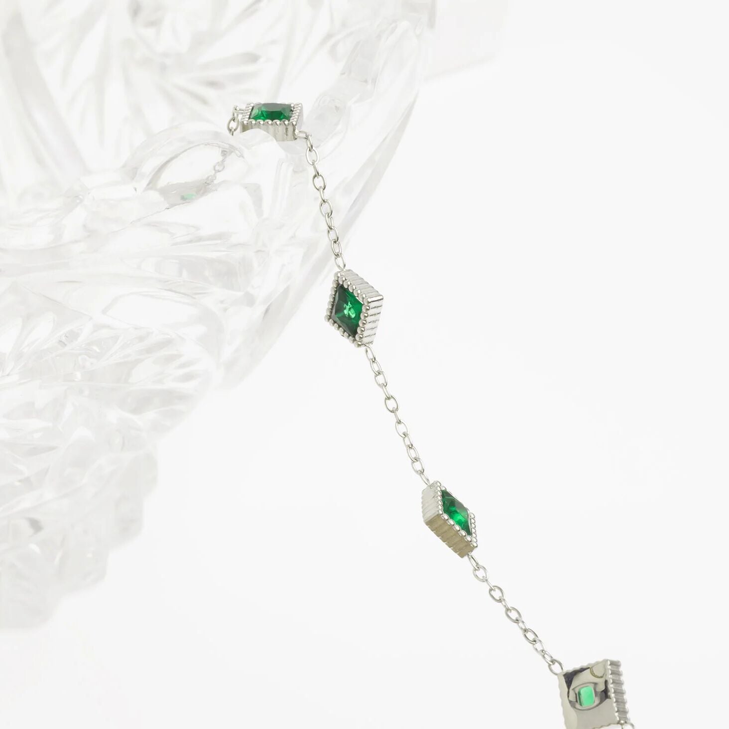 Silver bracelet with green gemstones on a textured white surface